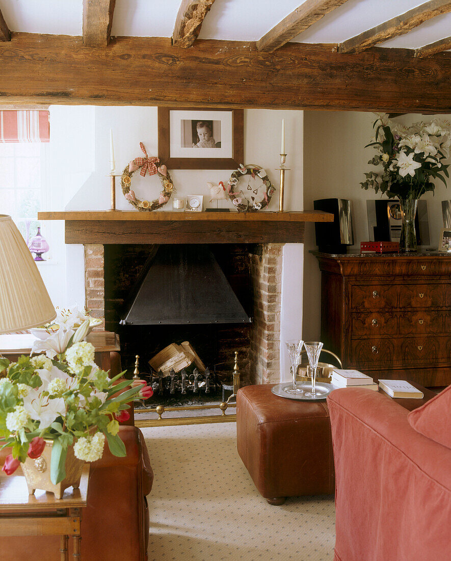 Kamin mit einem Holz-Kaminsims unter freiliegenden Holzbalken in traditionellem Wohnzimmer eines Landhauses