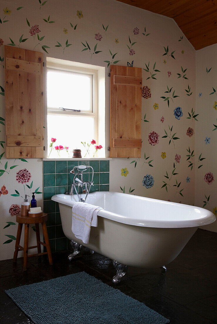 Holzfensterläden und handgemaltes Blumenbild von Ann-Louise R. über freistehenden Badewanne