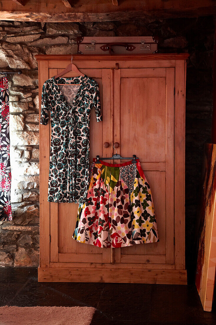 Kleid und Rock hängen an einem Kleiderschrank aus Holz