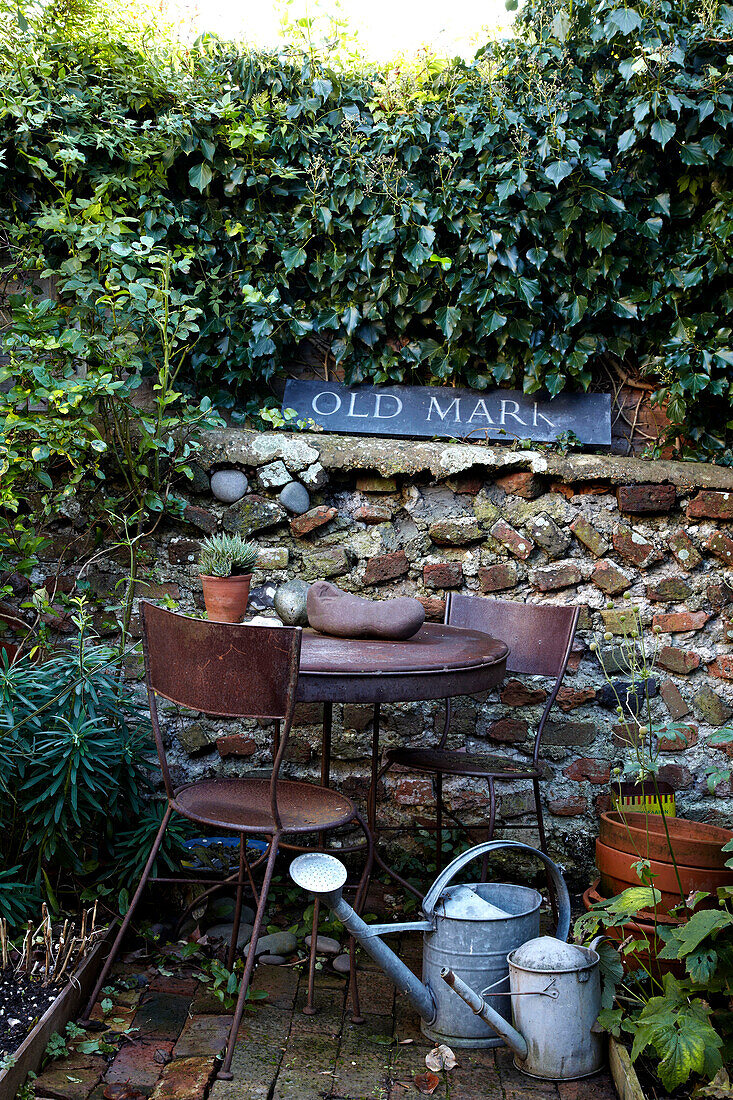 Rostiger Gartentisch, Stühle aus Metall und Gießkannen im Garten in Brighton, Sussex, UK