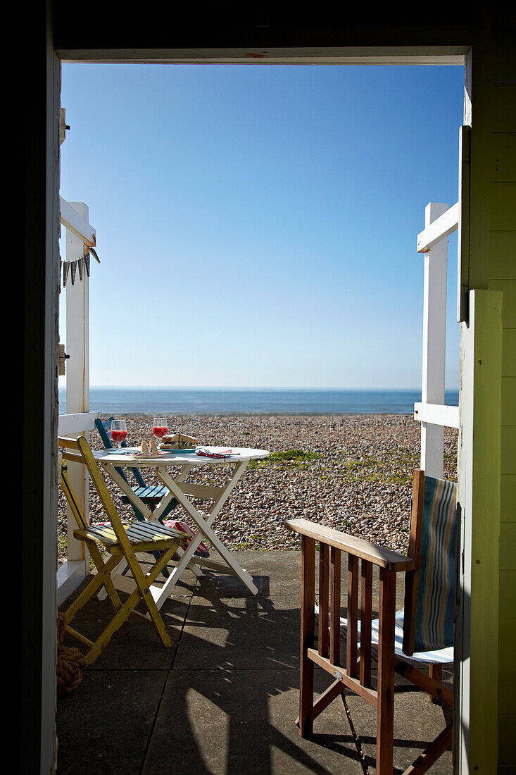 Blick durch die Tür einer Strandhütte auf den Kieselstrand an der Küste von West Sussex, England, UK