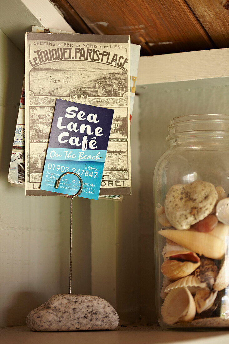 Postkarten im Kartenhalter daneben Glas mit Muscheln in Strandhütte in West Sussex, England, UK