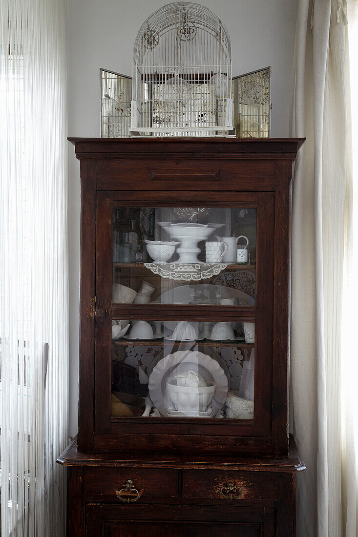 Metal bird cage on glass fronted cabinet holding china