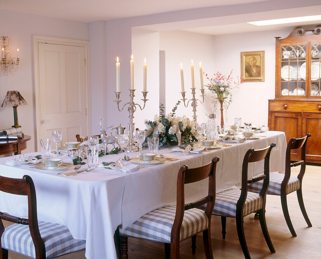 A traditional dining room table laid for dinner silver candelabra with lit candles wooden chairs with upholstered seats dresser