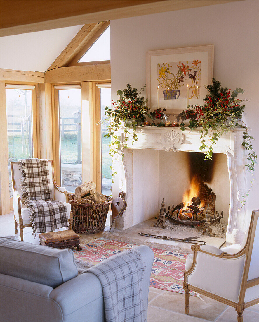 A traditional country sitting room with stone fireplace decorated for Christmas lit fire upholstered sofa armchair log basket