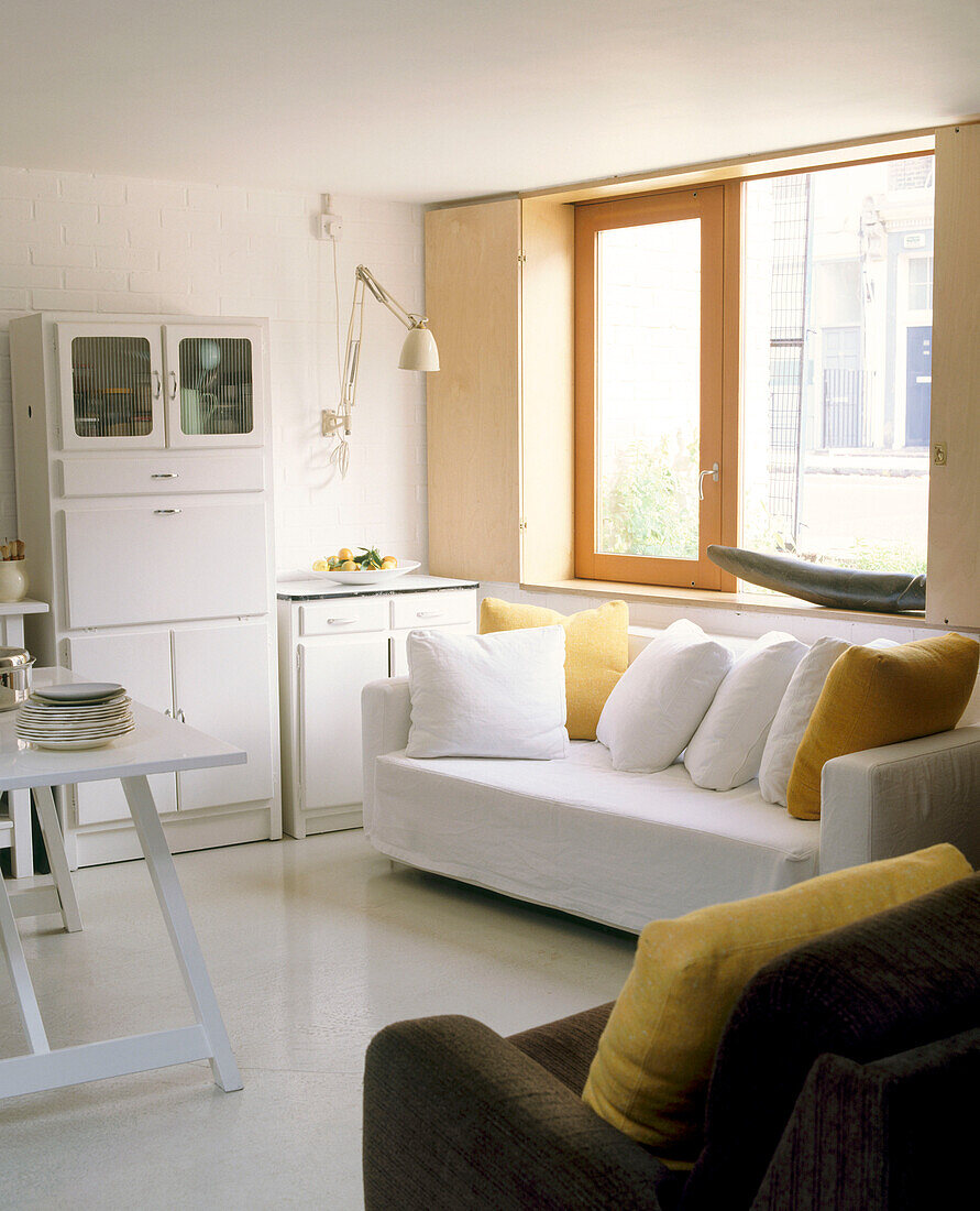 Modernes Wohnzimmer mit weißer Couch unter großem Fenster davor Tisch mit Tellerstapel