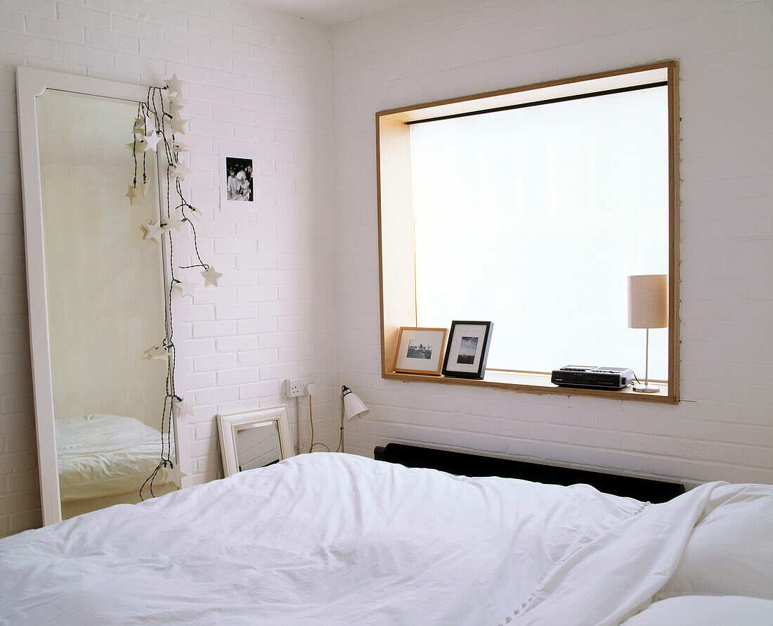 Ein modernes Schlafzimmer mit einem großen quadratischen Fenster, das das Bett mit einem großen Spiegel in voller Länge gegenüber beleuchtet