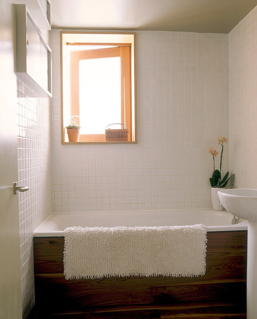 Ein modernes Badezimmer mit gefliesten Wänden und einem kleinen Fenster über der großen Badewanne
