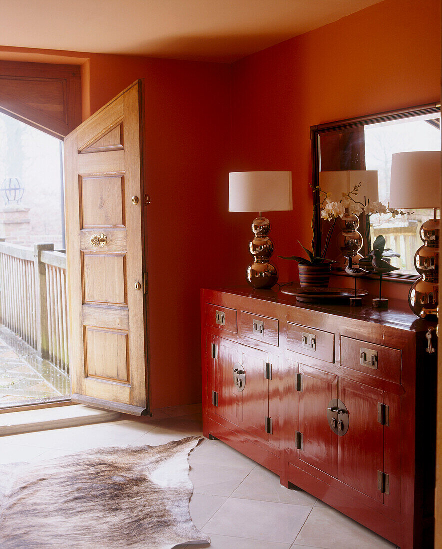A country style hallway by an open front door with a traditional antique style heavy dark wood cabinet