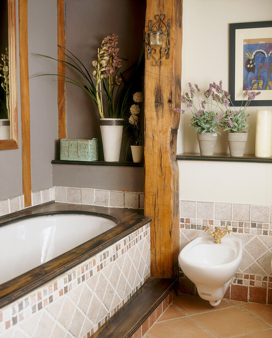 A modern bathroom with timber framed walls decorative tiles a mahogany wood framed bath a bidet plants and a painting