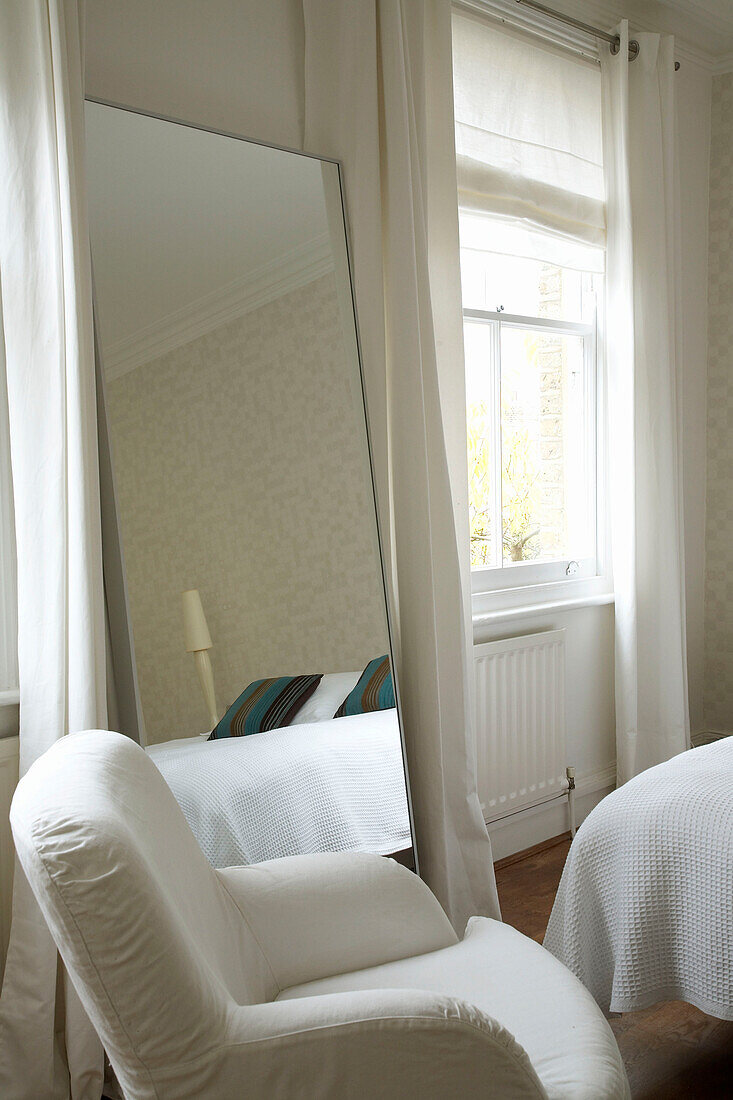 Modernes Schlafzimmer cremefarbenem Sessel und Bodenspiegel neben einem Fenster