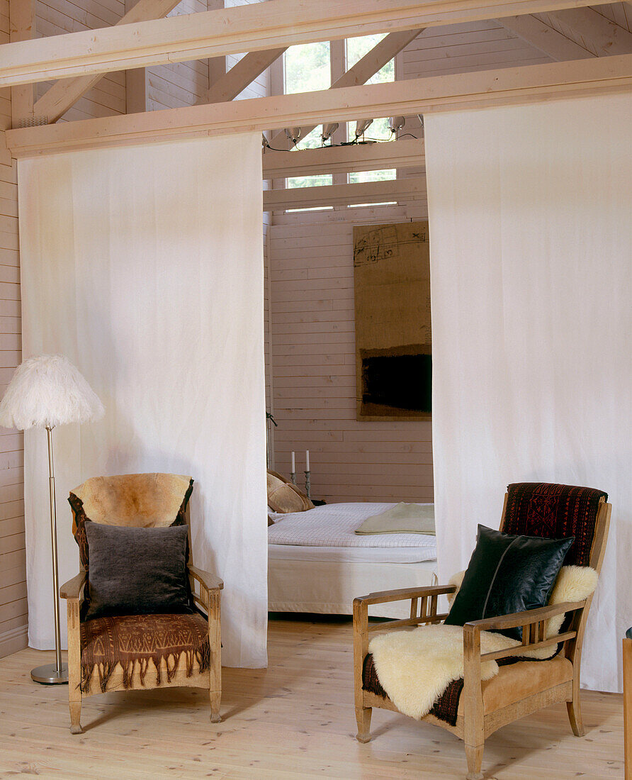 Country styled bedroom with a white screen in front of the bed and two armchairs in the foreground