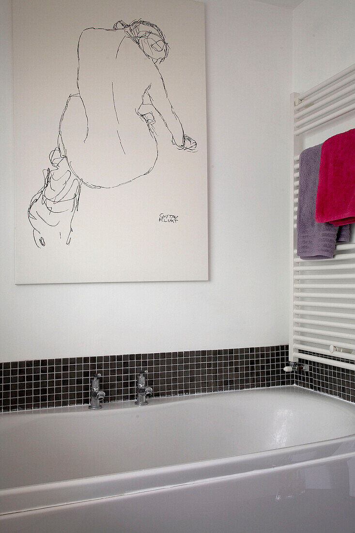 Detail of a modern bathroom bath with black and white poster above and towels on a rack