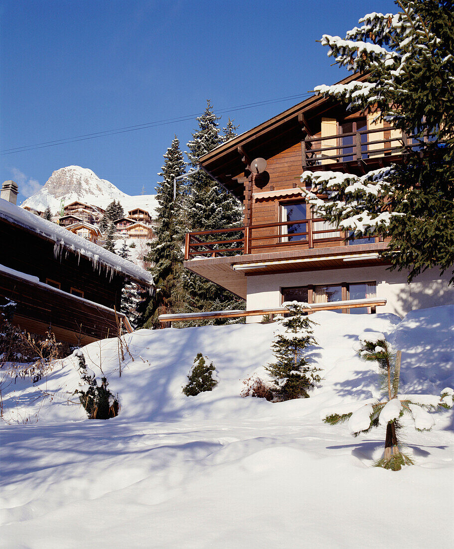 Außenansicht eines traditionellen Schweizer Holzchalets mit Schnee, Tannen und Bergen