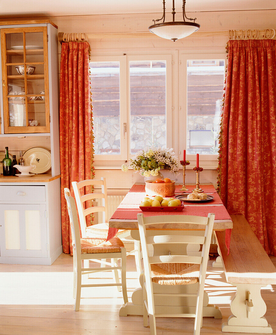 Offene Küche im Landhausstil mit Essecke, Holztisch, Stühlen, Sitzbank, Holzboden und roten Vorhängen