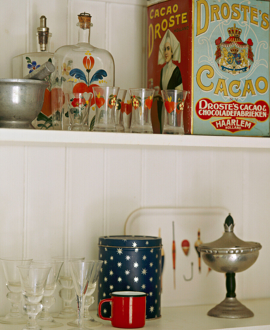 A detail of various items on shelves, painted glasses and bottles and old fashioned tins