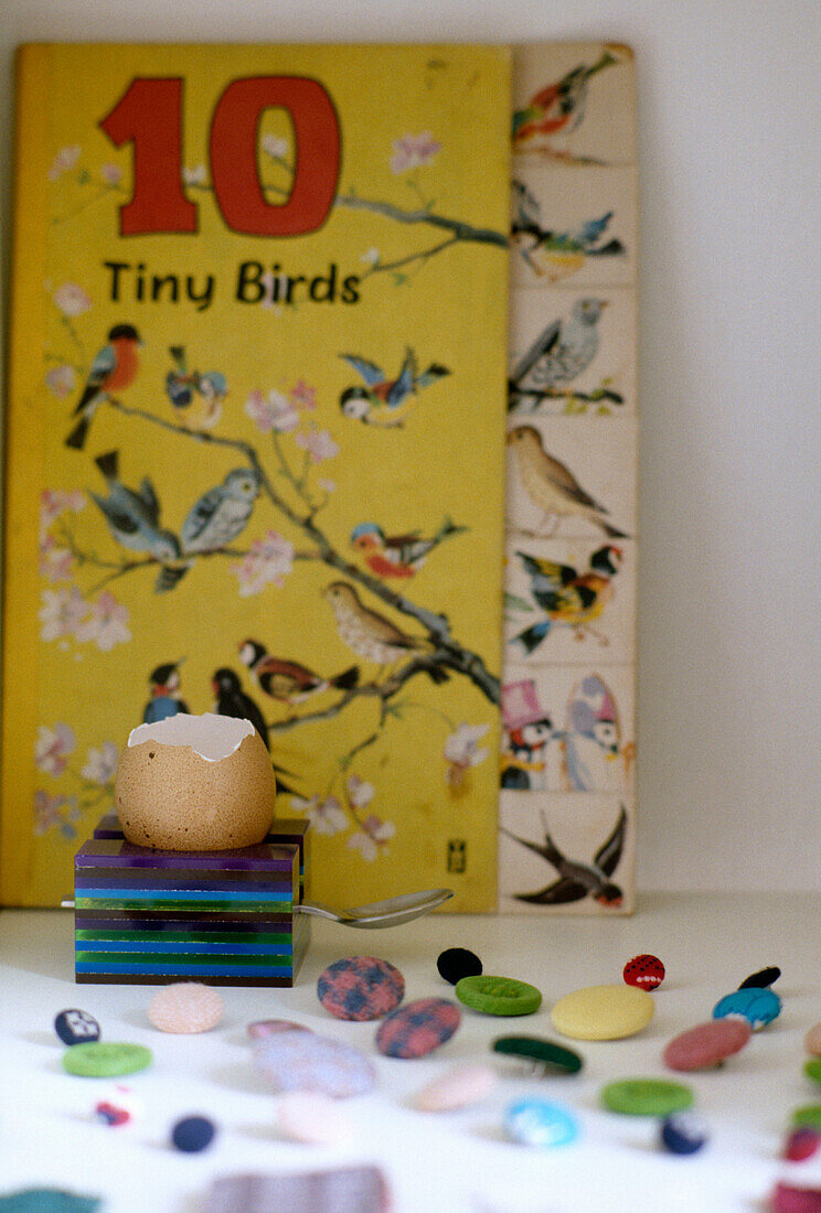 Ein Detail von einer Eierschale, in einer Tasse Knöpfe und ein Buch