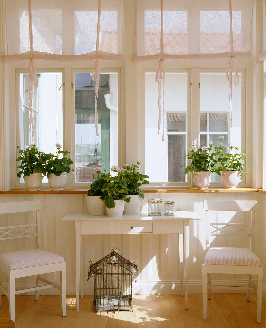 Ein Detail eines Wohnzimmers im Landhausstil in neutralen Farben mit Beistelltisch, Stühlen und Pflanzen auf dem Tisch und der Fensterbank