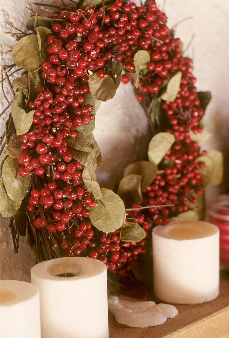 Detail eines Weihnachtskranzes aus roten Beeren mit Kerzen auf einem Kaminsims