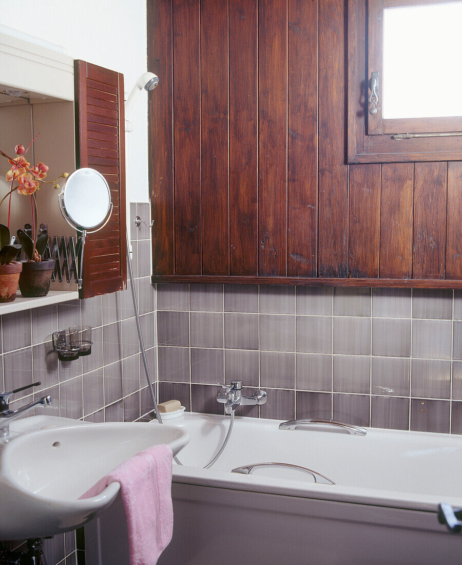 Ein Detail eines modernen Badezimmers mit holzverkleideter Badewanne, wandmontiertem Waschbecken und gefliester Wand