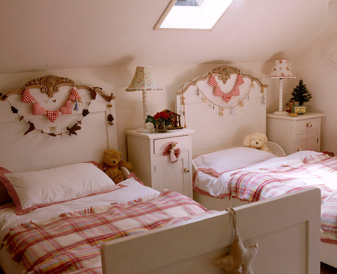 Ein traditionelles Kinderzimmer mit einem Oberlicht in einer Dachschräge und zwei Betten mit Weihnachtsdekoration an den Kopfteilen und auf den Nachttischen