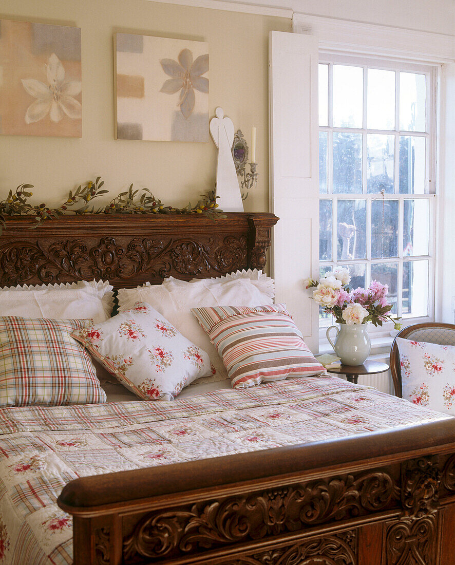 Ein traditionelles Schlafzimmer mit zwei Leinwandgemälden über einem verschnörkelten Holzbett mit geblümter Bettwäsche