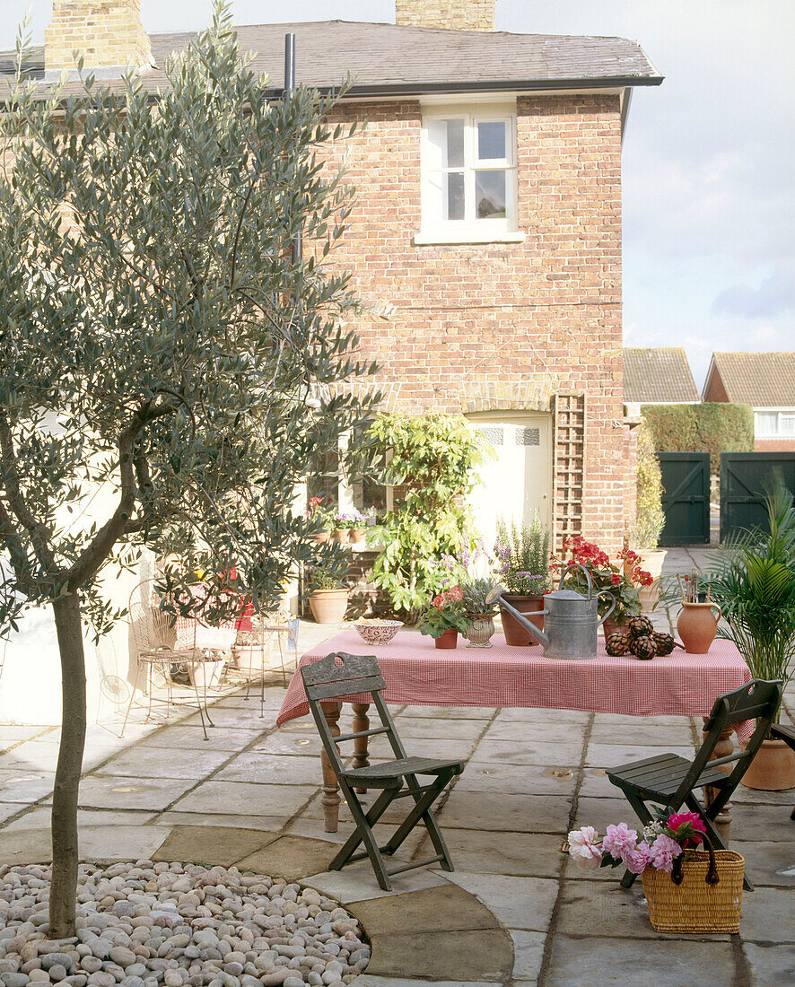 Außenansicht eines traditionellen Backsteinhauses mit einem Holztisch und Metallstühlen im gepflasterten Garten