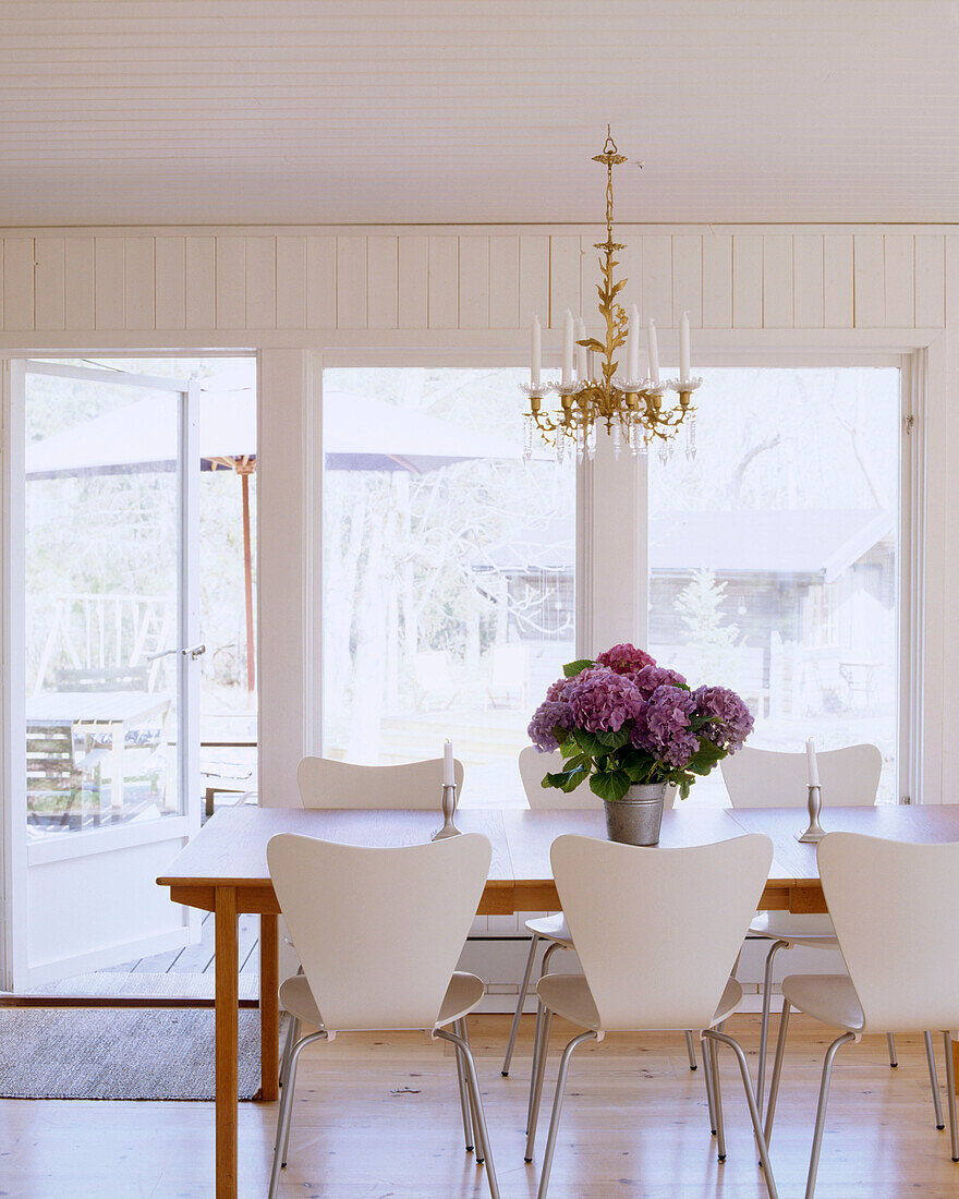 Ein modernes Esszimmer im skandinavischen Stil mit Esstisch aus Holz, weißen Stühlen und mauvefarbenen Blumen auf dem Tisch