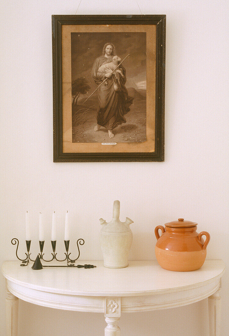 Close up detail of a framed portrait above a small semi circular table with candles and two small pots