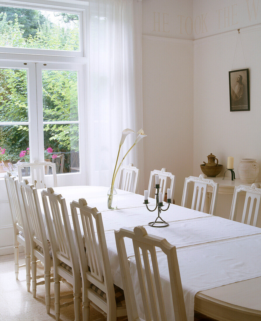 A large traditional dining room table surrounded by high backed wooden chairs with a large French door at the end