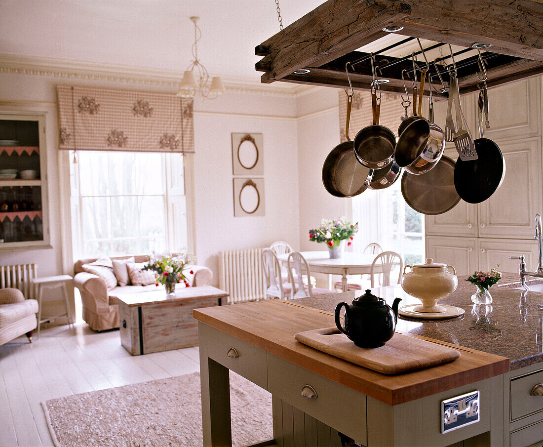 Saucepans hanging above worktop in open plan kitchen with teapot on chopping board