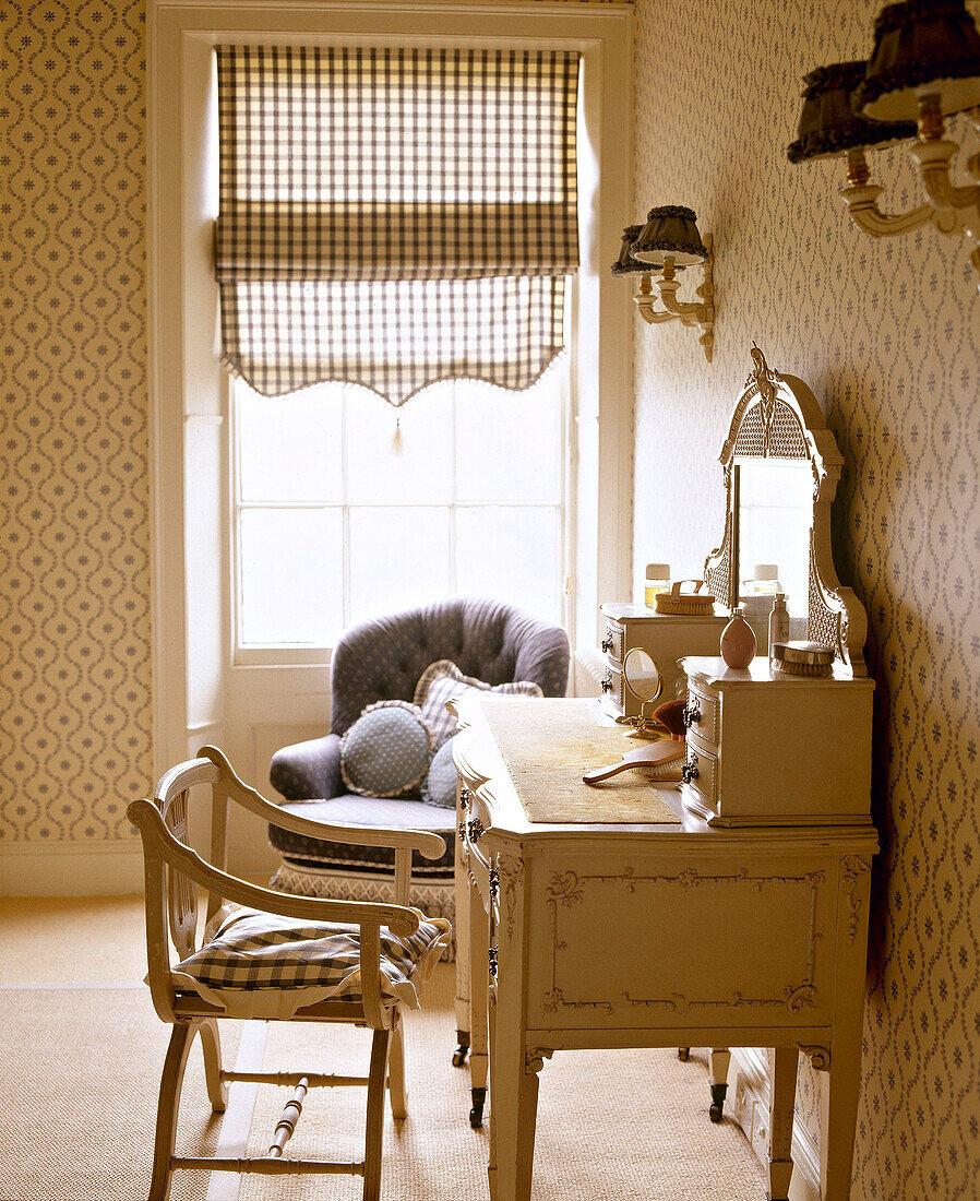 Schminktisch und Stuhl in einem Schlafzimmer mit gemusterter Tapete und Raffrollos am Fenster