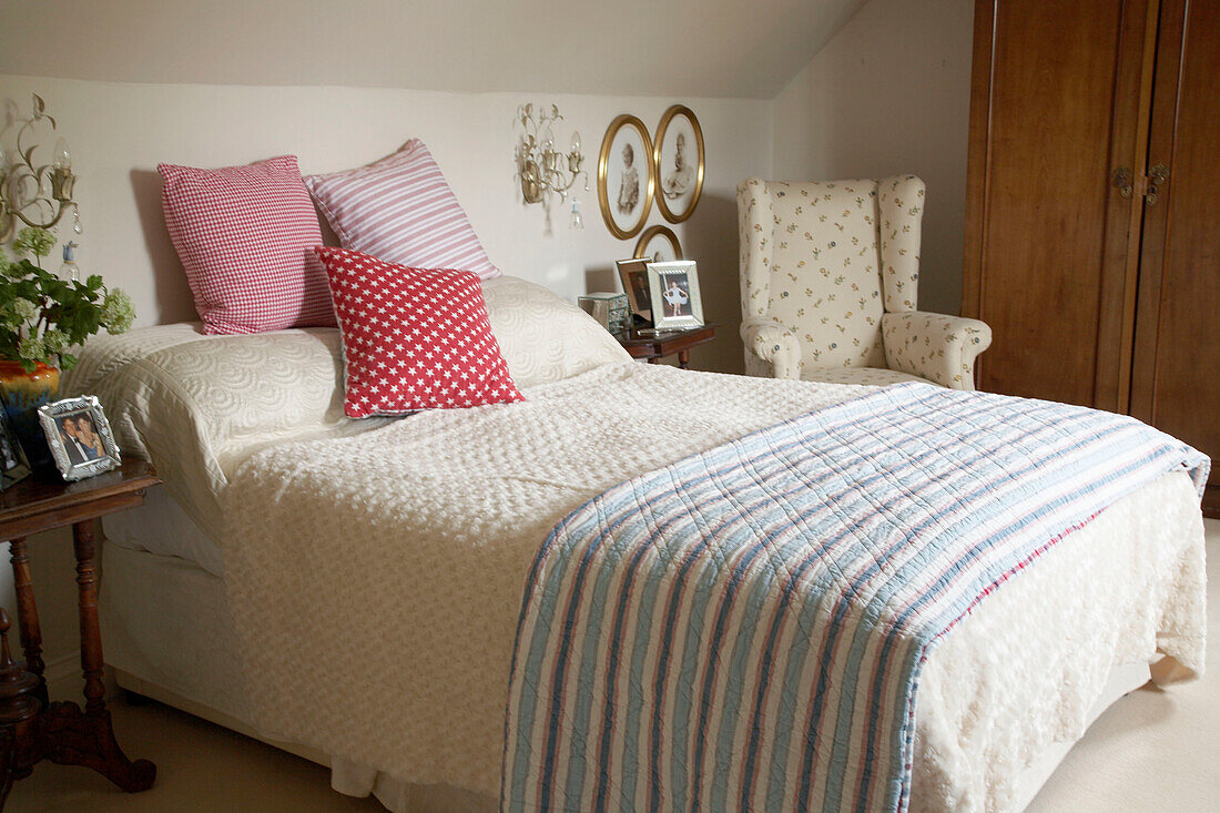Ein traditionelles Schlafzimmer im Landhausstil mit einem Doppelbett, einem gepolsterten Stuhl und zwei Nachttischen, Kissen und einer Überwurfdecke