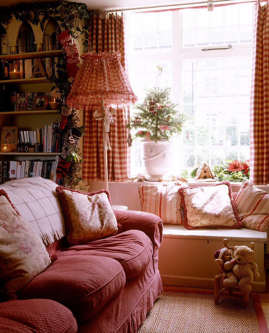 Traditionelles Wohnzimmer mit Sofa, rot kariertem Lampenschirm und Truhenbank vor Fenster mit rot karierten Vorhängen