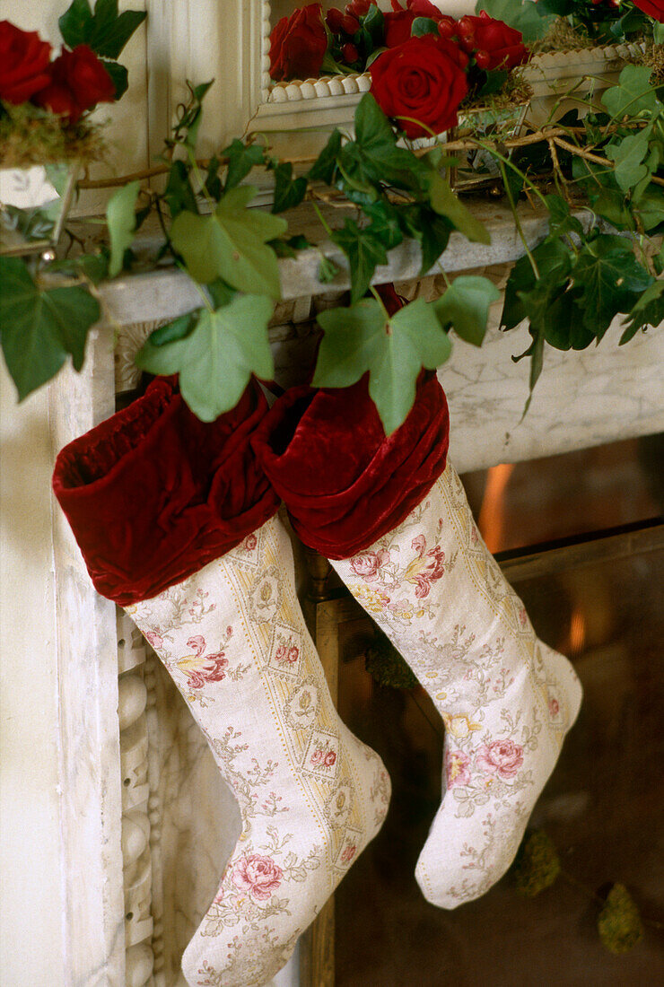 Close up detail of two traditional Christmas stockings hanging from a mantelpiece covered in ivy and roses