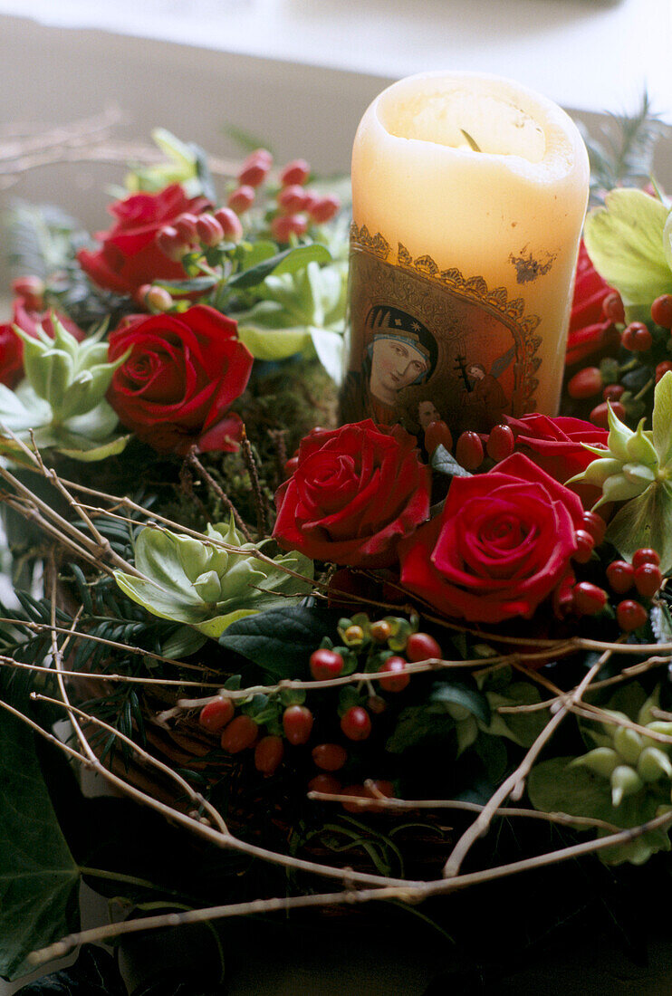Kerze mit religösem Motiv auf weihnchtlichem Gesteck mit roten Rosen