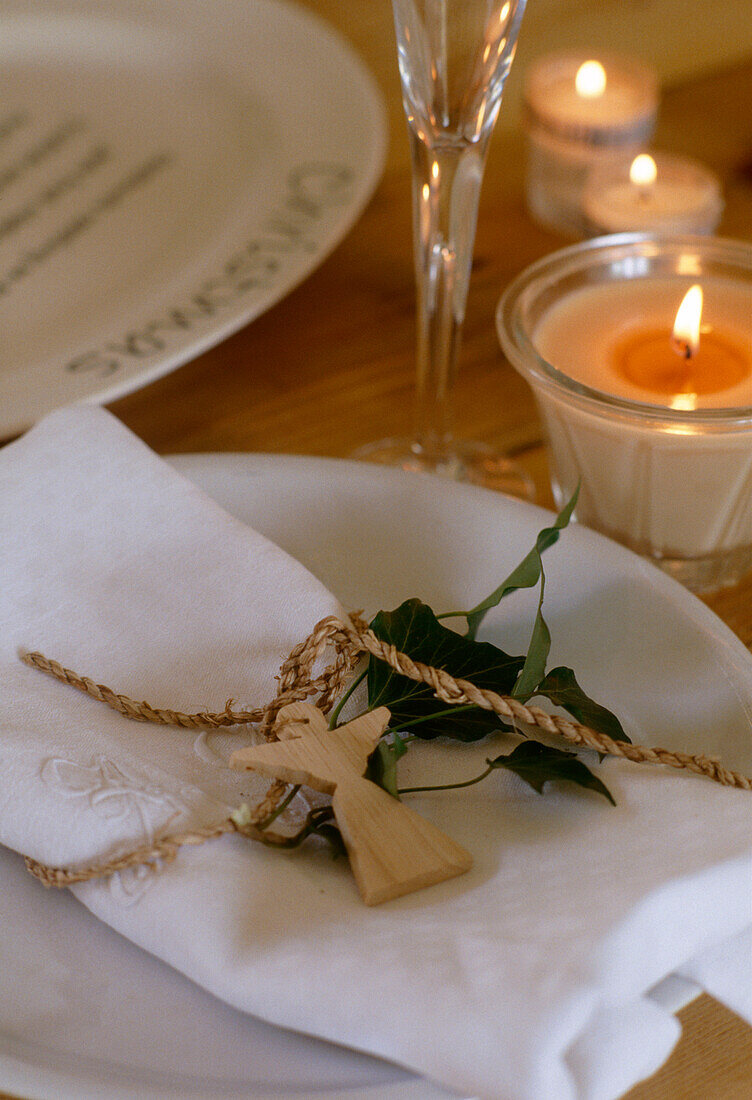 Close up detail of a traditional place setting with a wooden angel shaped ornament next to several potted candles