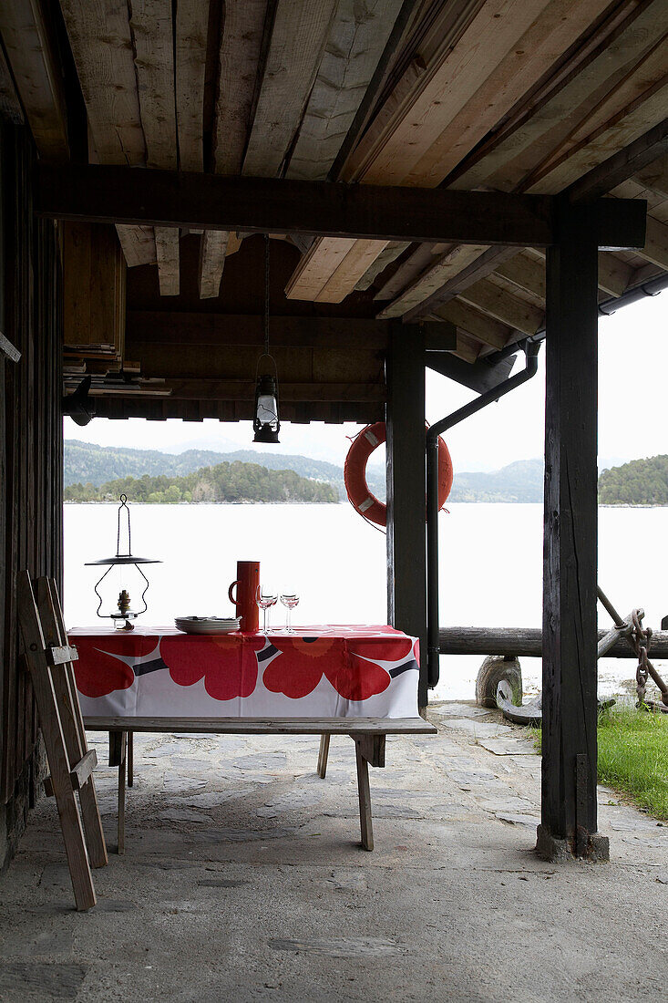 Tisch und Sitzbänke auf einer überdachten Terrasse mit Blick auf einen See