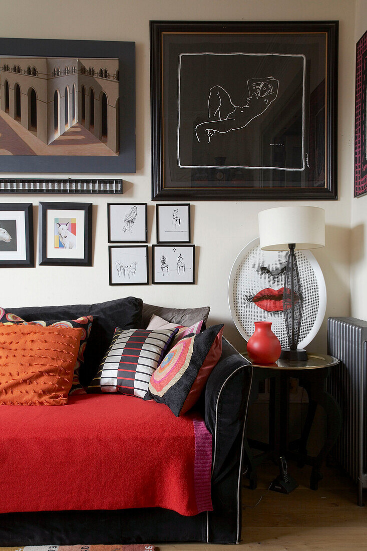 Sammlung von Kunstwerken über einem schwarzen Sofa mit roter Decke