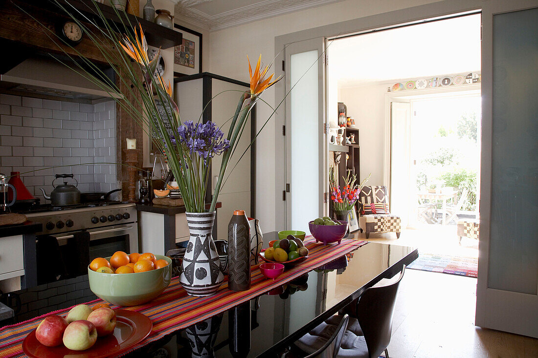 Blumenarrangement und Schalen mit Obst auf einem polierten Tisch in einer modernen Küche