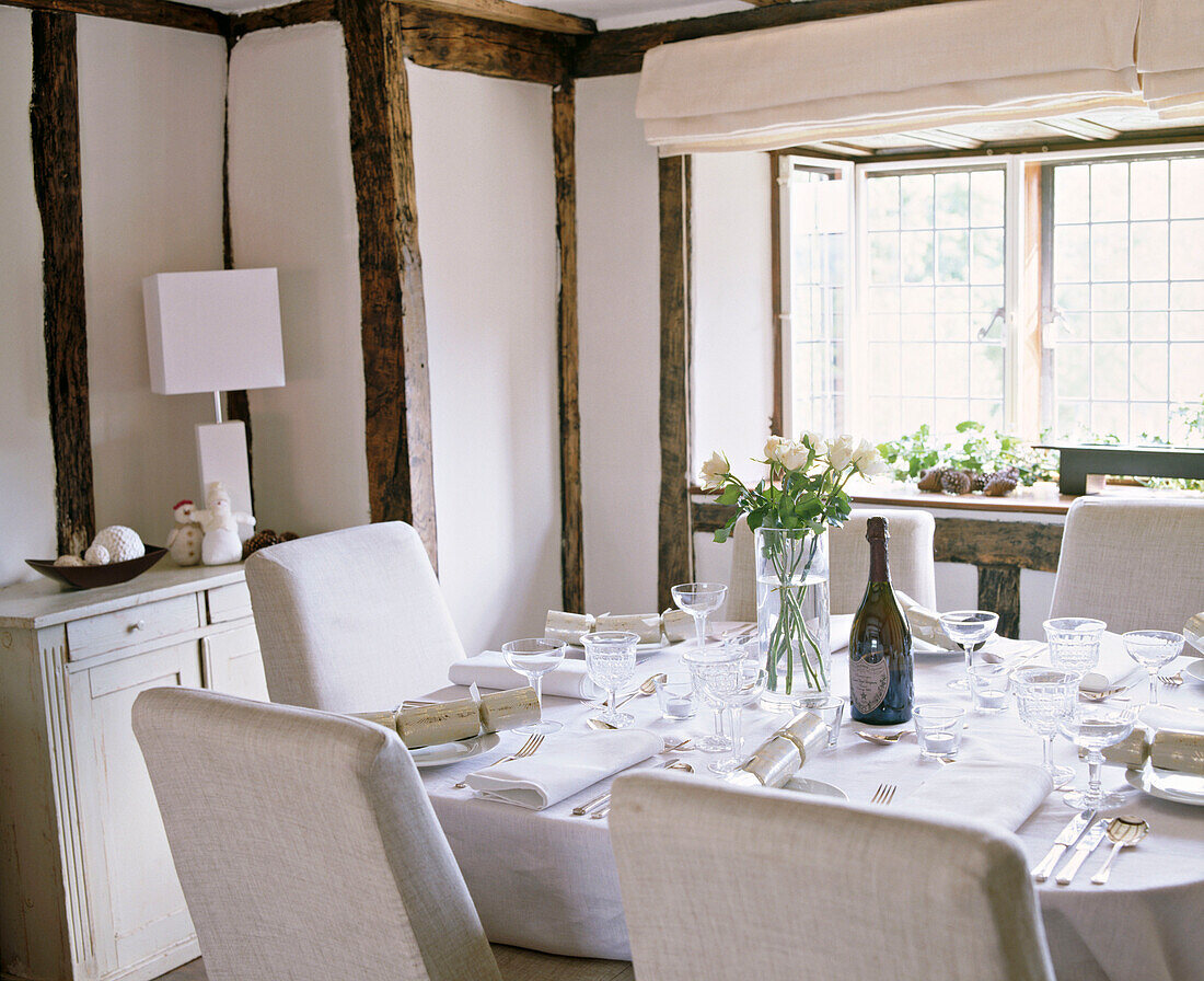 A country dining room decorated in neutral colours exposed beams table set for Christmas lunch upholstered chairs