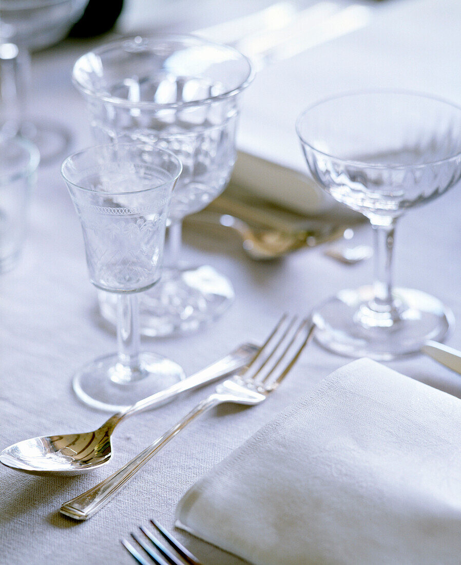 A detail of a dining table place setting silver cutlery wine glasses napkins