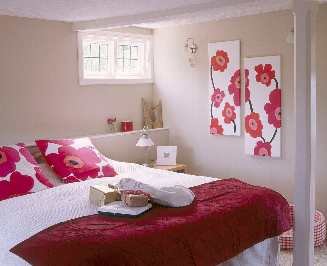 Double bed with red cover and pink floral patterned pillows with coordinated artwork