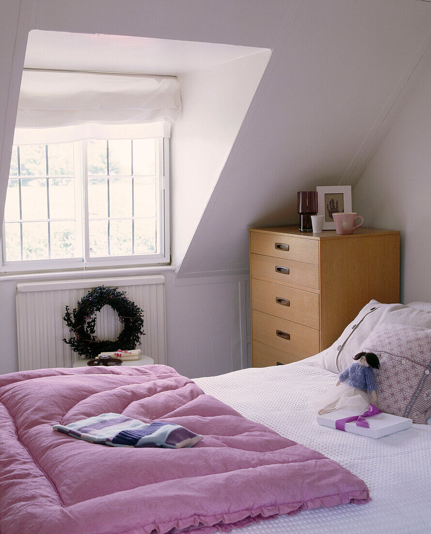 Ein modernes Schlafzimmer mit Doppelbett, Kommode, rosa Bettdecke und Fenster