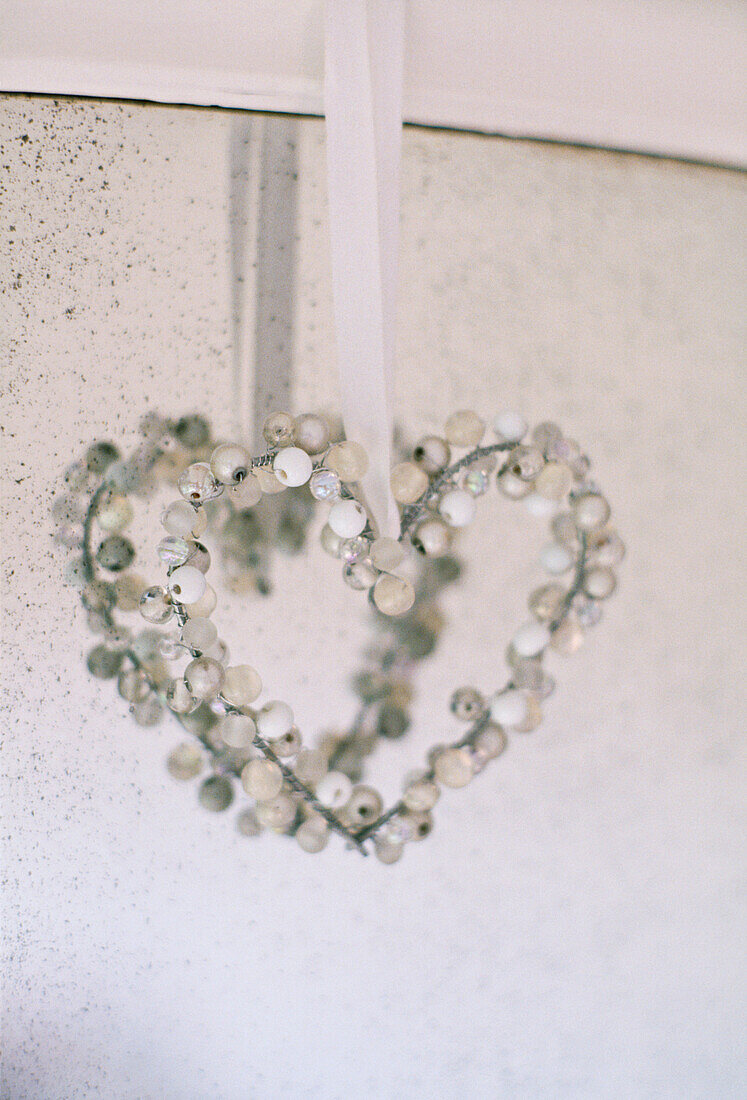 A detail of a beaded heart decorated hanging from ribbon