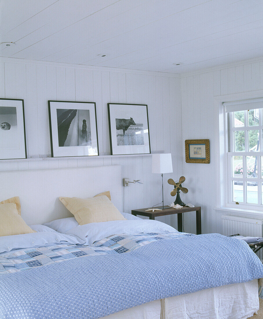 Fotografien auf einem Regal über einem Doppelbett mit blassblauem Bettbezug