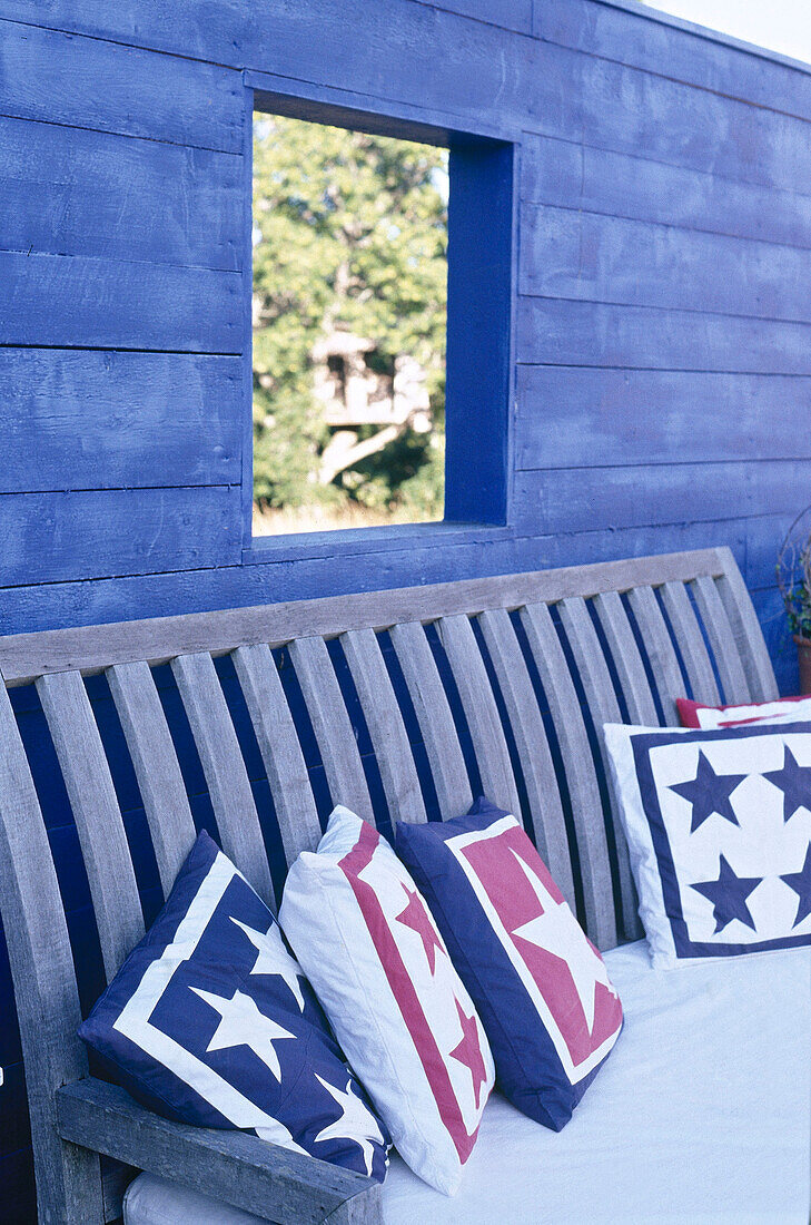 Holzbank und Kissen vor einer blau gestrichenen Holzwand