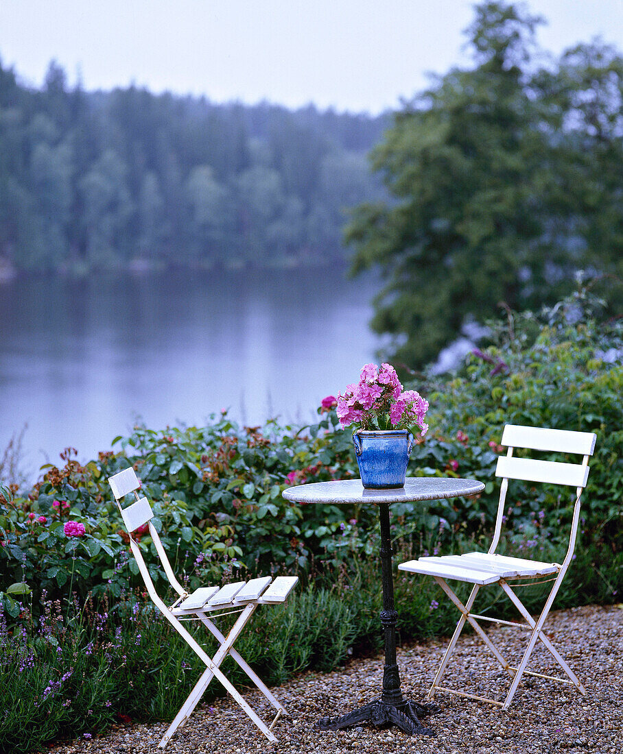 Terrassentisch und Stühle am bepflanzten Seeufer