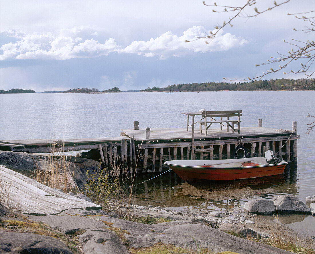 Seelandschaft mit einem an einem Holzsteg vertäuten Boot im Vordergrund