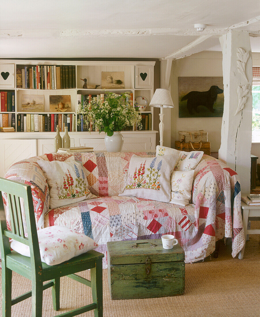 Ländliches Wohnzimmer gepolstertes Sofa mit Patchwork-Bezug, Holztruhe, bemaltes Holzregal, Lampe, Blumenarrangement
